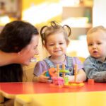 cute babies play with carer or babysitter in nursery or kindergarten